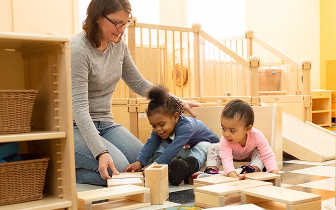 teacher guiding two babies with mini unit blocks indoors