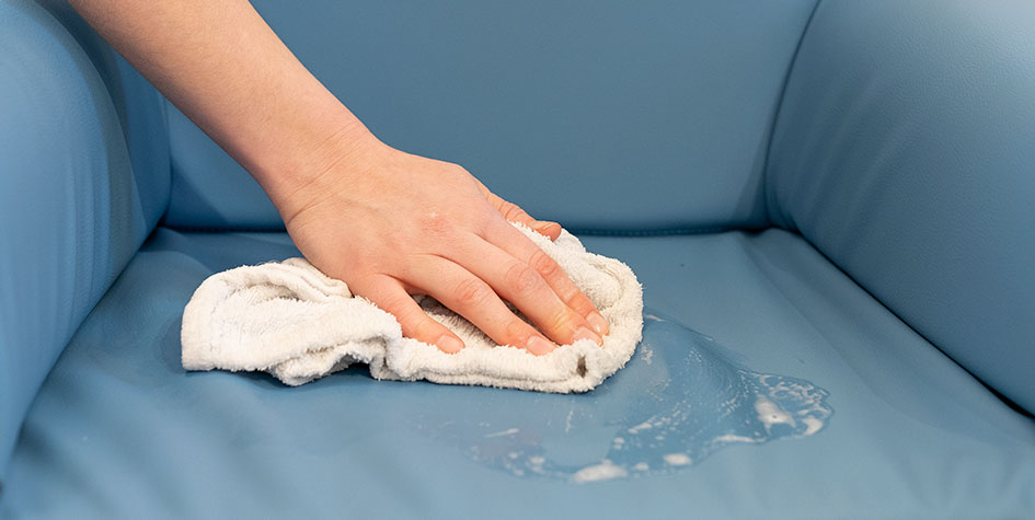 A hand with a rag, wiping a sofa.
