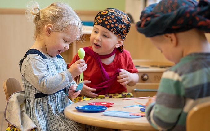 Three young childen dressed up playing around a table