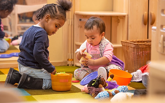 Young child and toddler role playing with dolls and dolly dishes