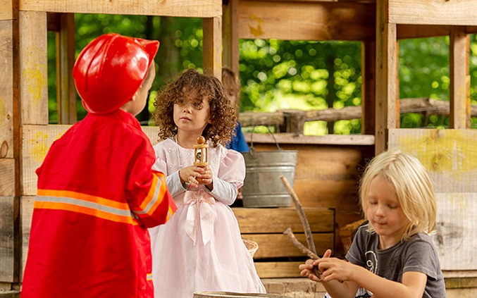 Three young children dressed up and engaged in outdoor role play