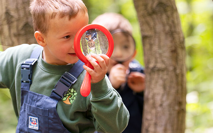 Two young boys using magnifying glasses to explore nature in a forest environment.