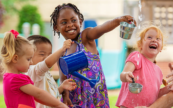 A group of children laughing and playing with water using cups and containers outside.