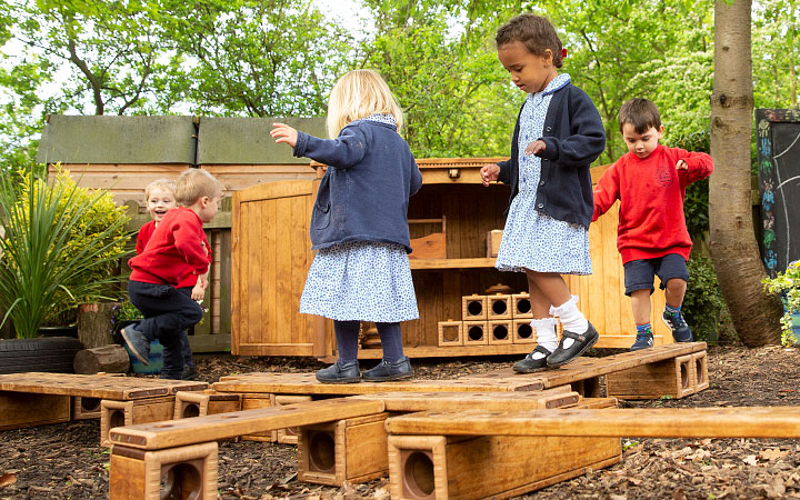 Nursery and reception children wearing blue and red school uniforms and blancing on an obstical course constructed from Outlast blocks and planks.