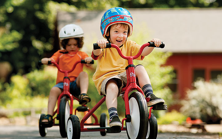 Reception aged boys wearing orange and yellow shirts and pedalling red trikes.