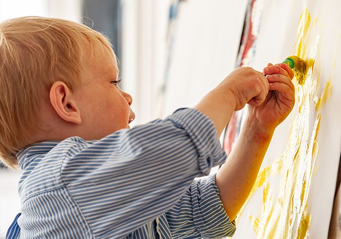 A young child is standing in front of an easel and painting on it