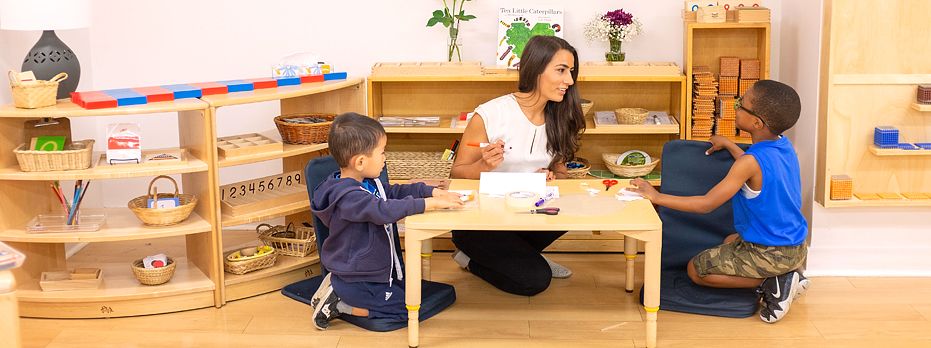 A teacher at a low table with two young children kneeling