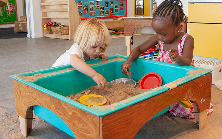 two girls playing with sand in a sand and water table