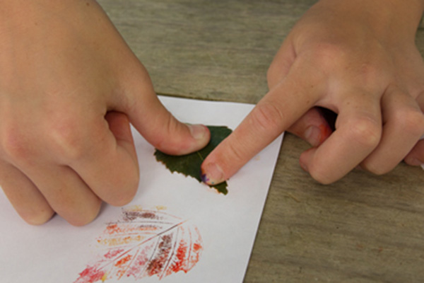 child‘s hands pressing leaf onto paper