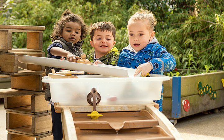 A wider view of three children engaged in hands-on water play. This Outlast Cascade allows for exploration and interaction in an outdoor learning environment.