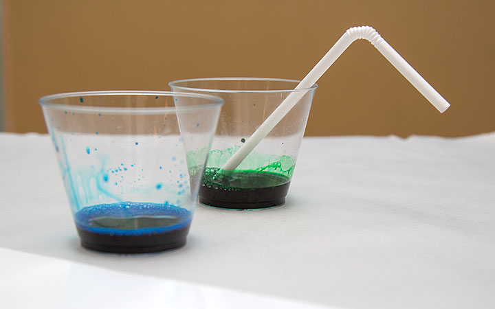 one clear cup with dark blue and one with dark green liquid and a straw