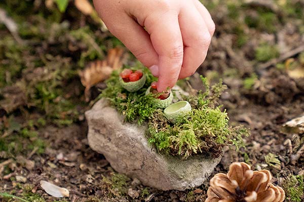 childs hand placing berries into acorn caps