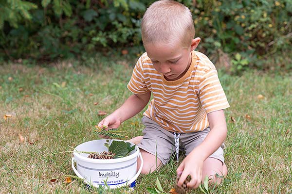 boy collecting nature items into bucket