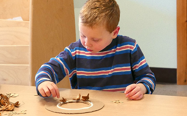 Boy placing beech nut husks into glue on cardboard circle