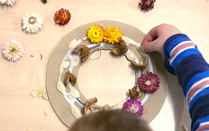 Overhead view of boy sticking nature items into glue on wreath