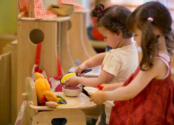 two children playing in the home corner with a doll high chair