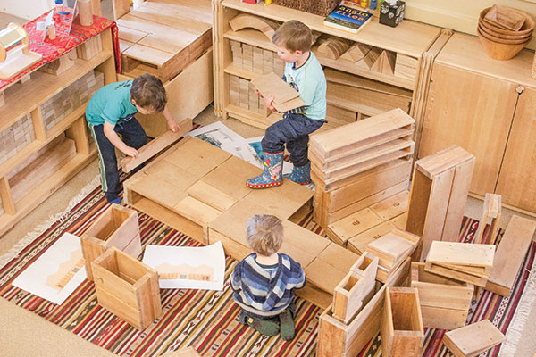 three children playing with wooden hollow blocks in the block corner of a nursery