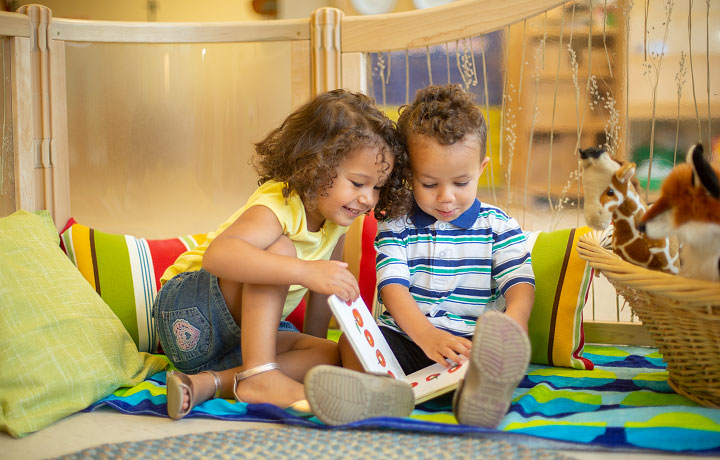 Two small children reading in a book in a cosy corner