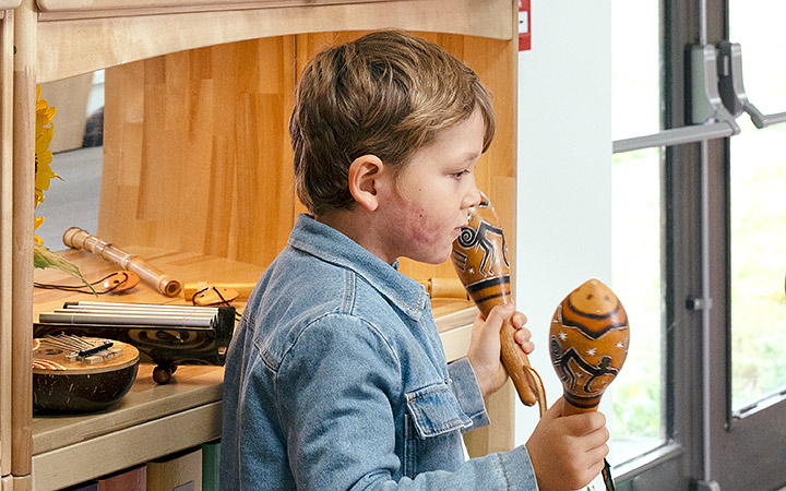 A boy wearing a denim jacket and shaking two African rattles