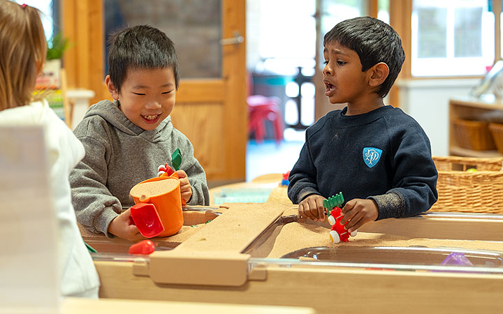 Two boys playing with sand in a tuff tray style pan