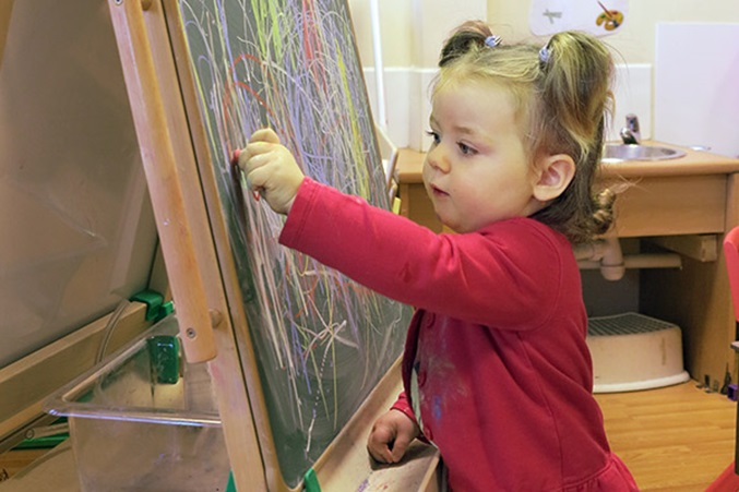 a boy mark making with chalk on an easel