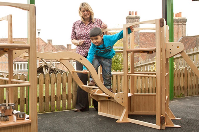 a boy balancing on a playframe with a teachers help