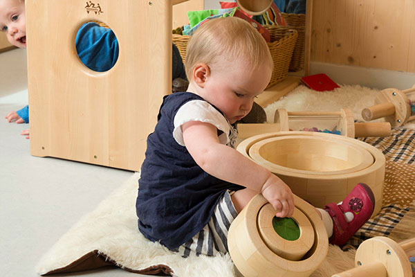 baby playing with simple wooden toys in front of a baby shelf