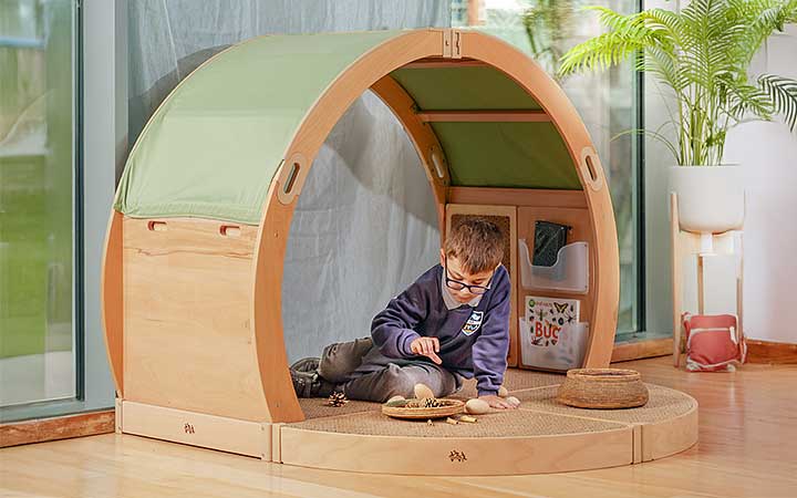 A boy at primary school doing an activity in a solid wood regulation space with a cosy fabric roof.