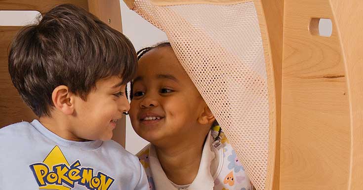 Two children in a solid wood regulation space laughing together.