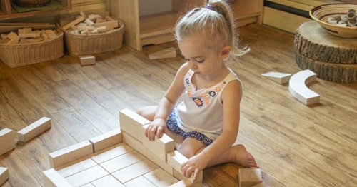A girl is building a house out of wooden unit blocks