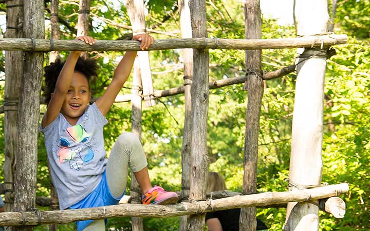 A child climbing on a natural wooden outdoor climbing frame