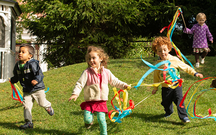 Four young children are running over a lawn with colourful streamers in their hands
