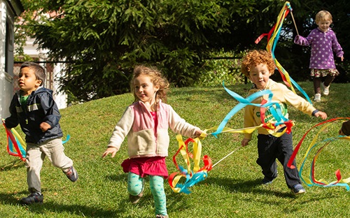 Several children are running over a lawn with streamers