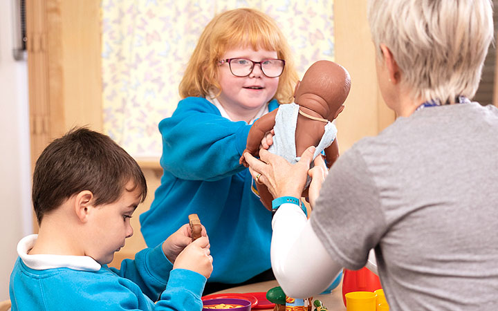 teacher handing a doll to an SEN child