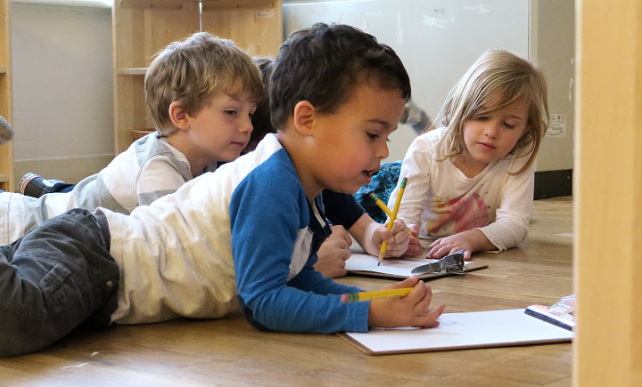 Three nursery-aged children working with planning boards on the floor