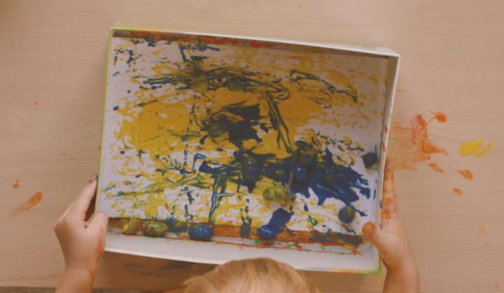 Child rolls acorns with blue paint into a box