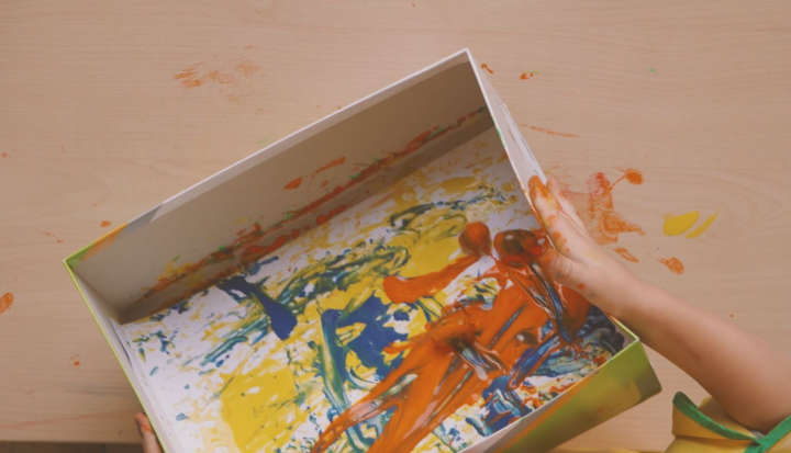 Child rolling orange acorns over paper in a box