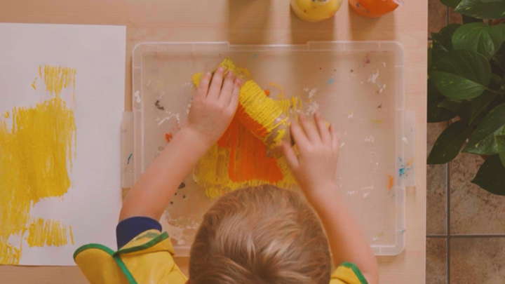 child rolling carboard tube wound with string on plastic tray covered in paint