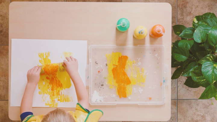 child rolling paint on paper using cardboard tube wound with string