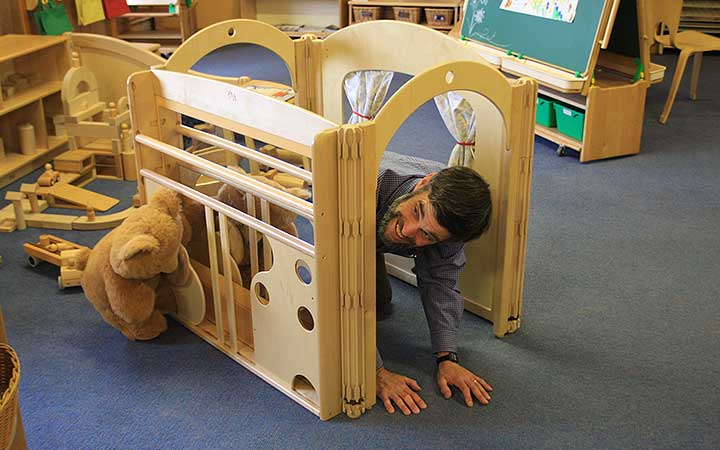 A teacher joking around and playing with toddler furniture in jest.