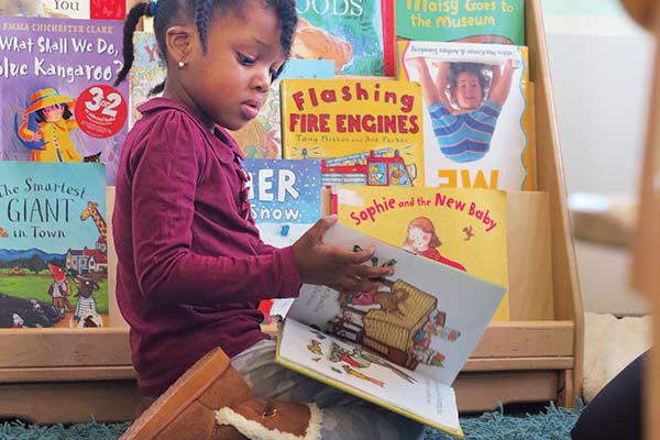 girl reading book in front of book shelf