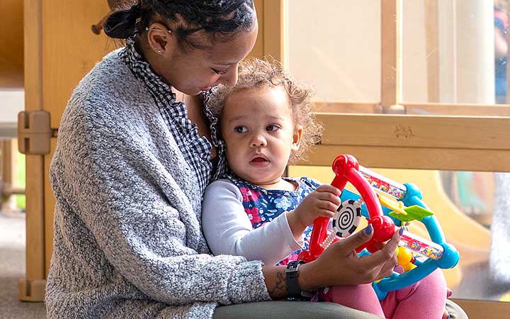 Caring teacher with a relaxed child on her lap playing with a toy.