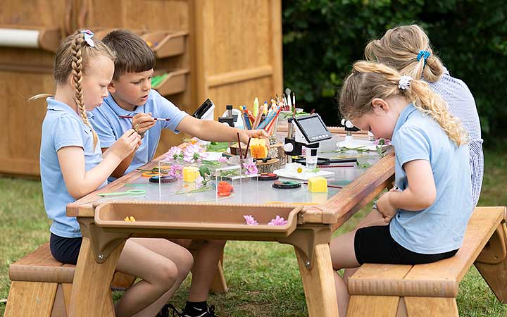 Four children sitting at an outside table doing crafts.