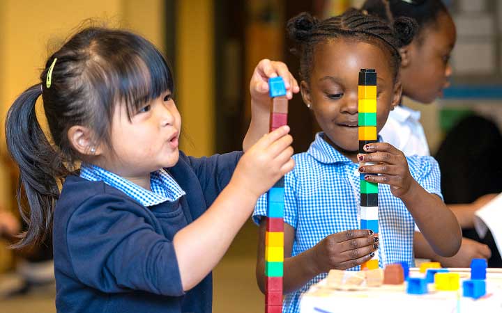 Three children smiling and building duplo towers.
