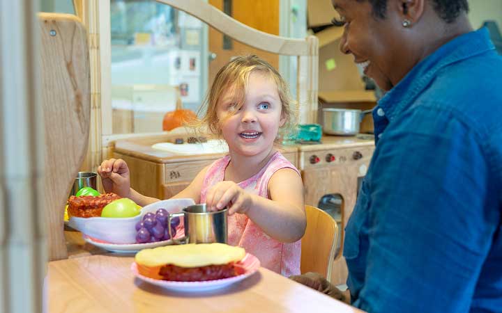 Teacher smiling and playing alongside child.