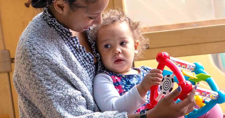 Teacher holding a child playing with a toy.