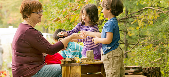 two children show nature objects to their teacher
