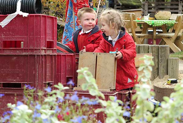 two kindergarten children playing with found materials outdoors