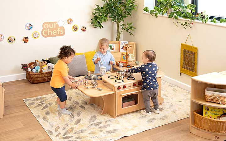 A role play area for babies and toddlers, with three toddlers playing at the Kitchen Island.