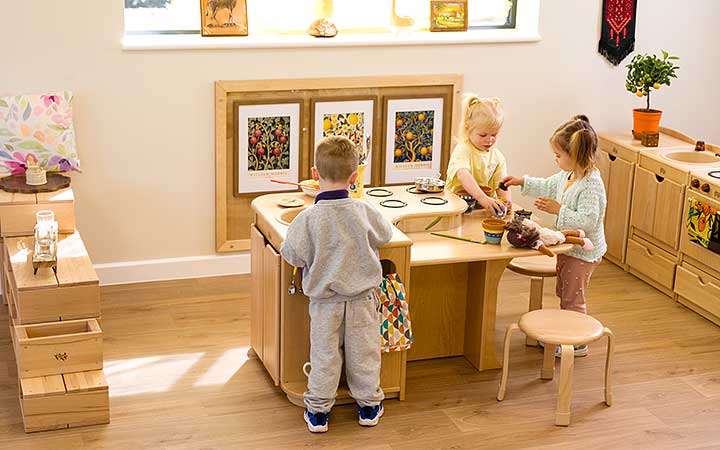 A preschool home corner with three children playing together at the Kitchen Island role play unit.